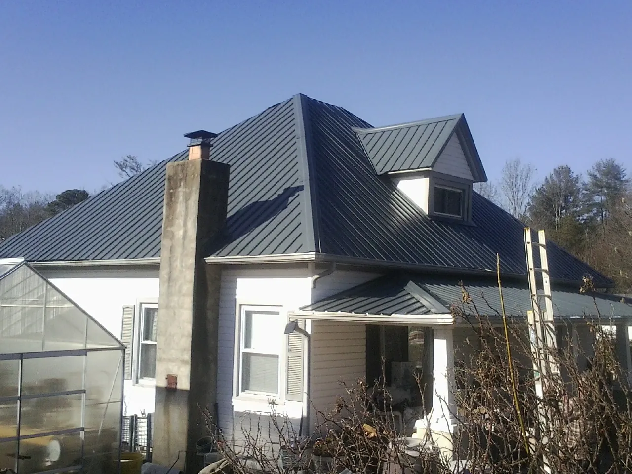 Dark blue standing seam metal roof on a white farmhouse with dormer in Rockaway Beach