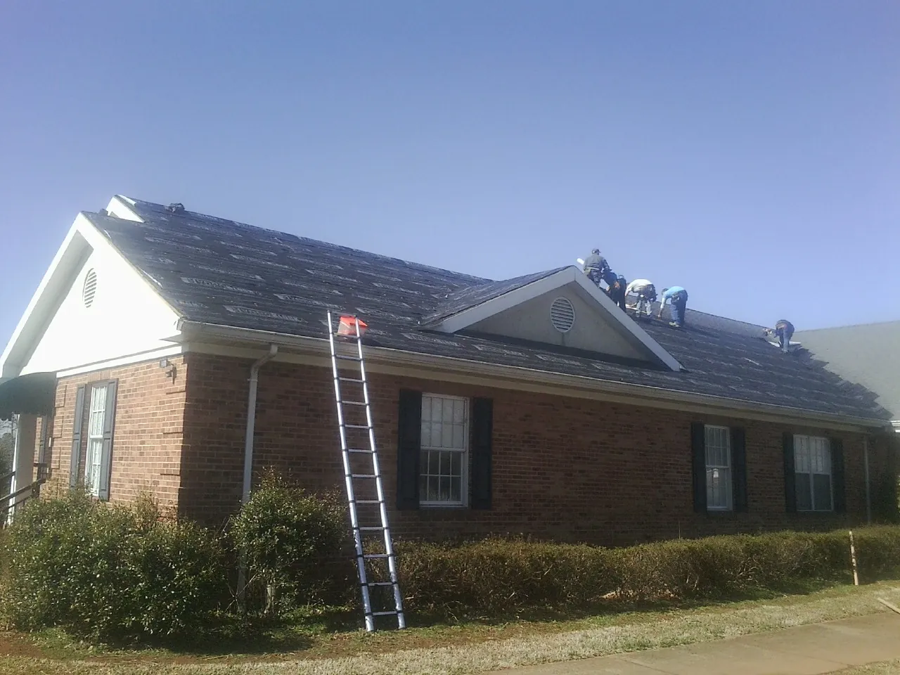 Crew tearing shingles off a brick ranch roof with a ladder set — Emergency Roof Repair work by our crew in Rockaway Beach