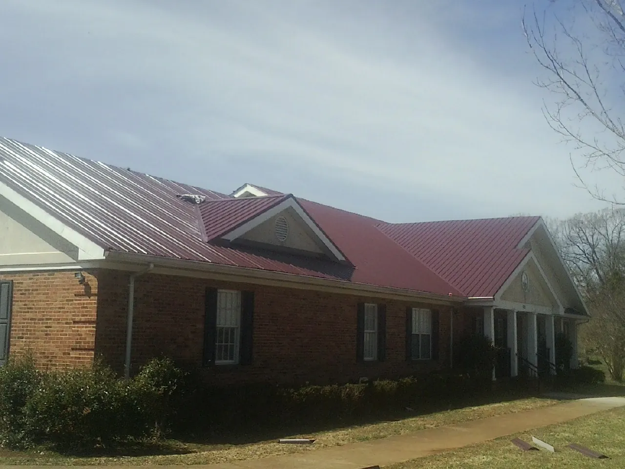 Red metal roof with gabled entries on a long brick building, from a Hail Damage Roof Repair job in Rockaway Beach