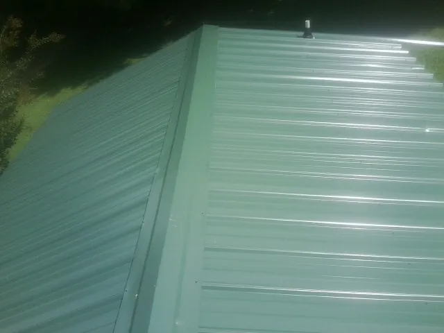 New green metal panels meeting at the ridge of a roof — Flat Roof Repair work by our crew in Rockaway Beach