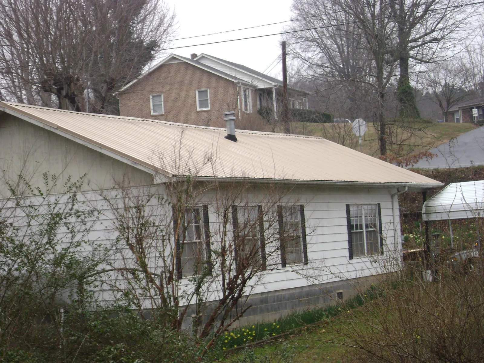 Tan metal roof on a white sided house set into a hillside — Commercial Roofing by Roofing Brothers in Rockaway Beach