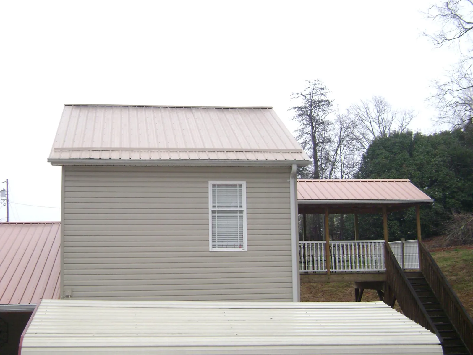 Tan metal roofs on a two story addition and attached porch, from a Roof Replacement job in Rockaway Beach
